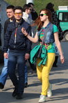 Straßenmode in Minsk. 04/2013. Teil 2 (Looks: blaue Jacke, blaue Jeans, Sonnenbrille, blaue Jeans Weste, grünes bedrucktes Top, gelbe Jeans, gelbe Hoch geschnittene Sneakers, rote Haare)