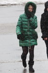 Street fashion under the snowfall. December 2018 in Minsk (looks: green jacket, black tights)