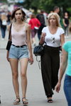 Sierpień 2018. Moda uliczna w Soligorsku (ubrania i obraz: top różowy, jeansowe szorty błękitne, rzemień czarny, sandały czarne, top biały)