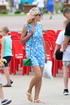Straßenmode in Saligorsk. 08/2018 (Looks: blonde Haare, himmelblaues Mini Kleid mit Blumendruck, grüne Handtasche, weiße Sandaletten)