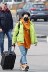 Straßenmode in Minsk. 03/2020 (Looks: hellgrüne gesteppte Jacke, orange Kapuzenpullover mit Slogan, himmelblaue Jeans, weiße Sneakers)