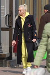 Moda uliczna w Mińsku. 03/2020 (ubrania i obraz: bluza z kapturem żółta, spodnie sportowe żółte, palto czarne, buty sportowe białe, blond (kolor włosów), koński ogon (fryzura))