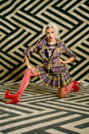 Kampania Vivienne Westwood SS21 (ubrania i obraz: garnitur damski (żakiet, spódnica) w kratę wielokolorowy, botki damskie czerwone, rajstopy w kolorze fuksji z podartymi nogawkami, blond (kolor włosów))