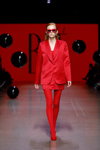 Pokaz BAE by Katya Shehurina — Riga Fashion Week SS24 (ubrania i obraz: garnitur damski (żakiet, spódnica) czerwony, rajstopy czerwone, półbuty czerwone, okulary przeciwsłoneczne, rude włosy)