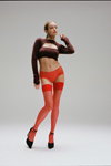 Kampania bielizny Chantelle FW 23/24 (ubrania i obraz: pończochy czerwone, krótki pulower brązowy, półbuty czarne, figi czerwone)